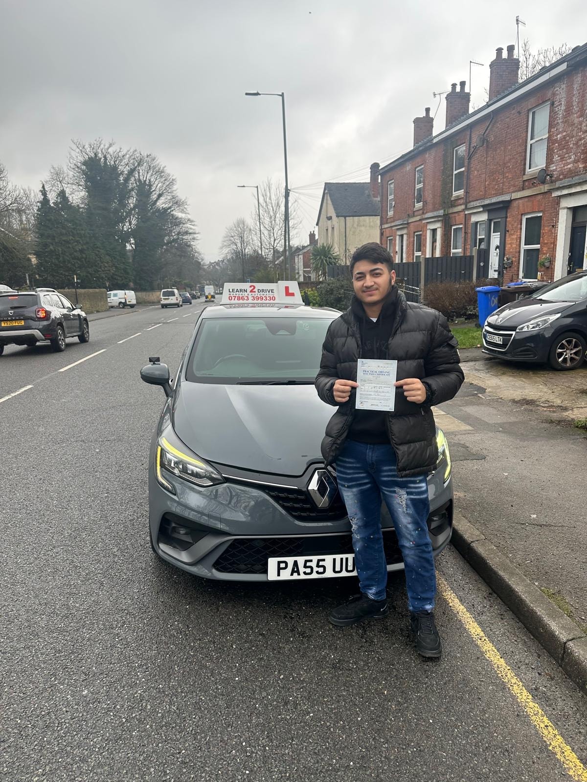 Student holding pass certificate in front of a Learn 2 Drive car