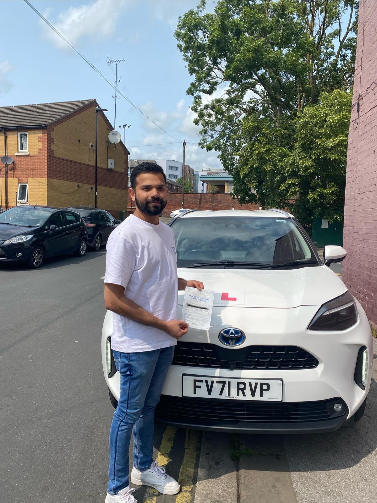 Student holding pass certificate next to a Learn 2 Drive car