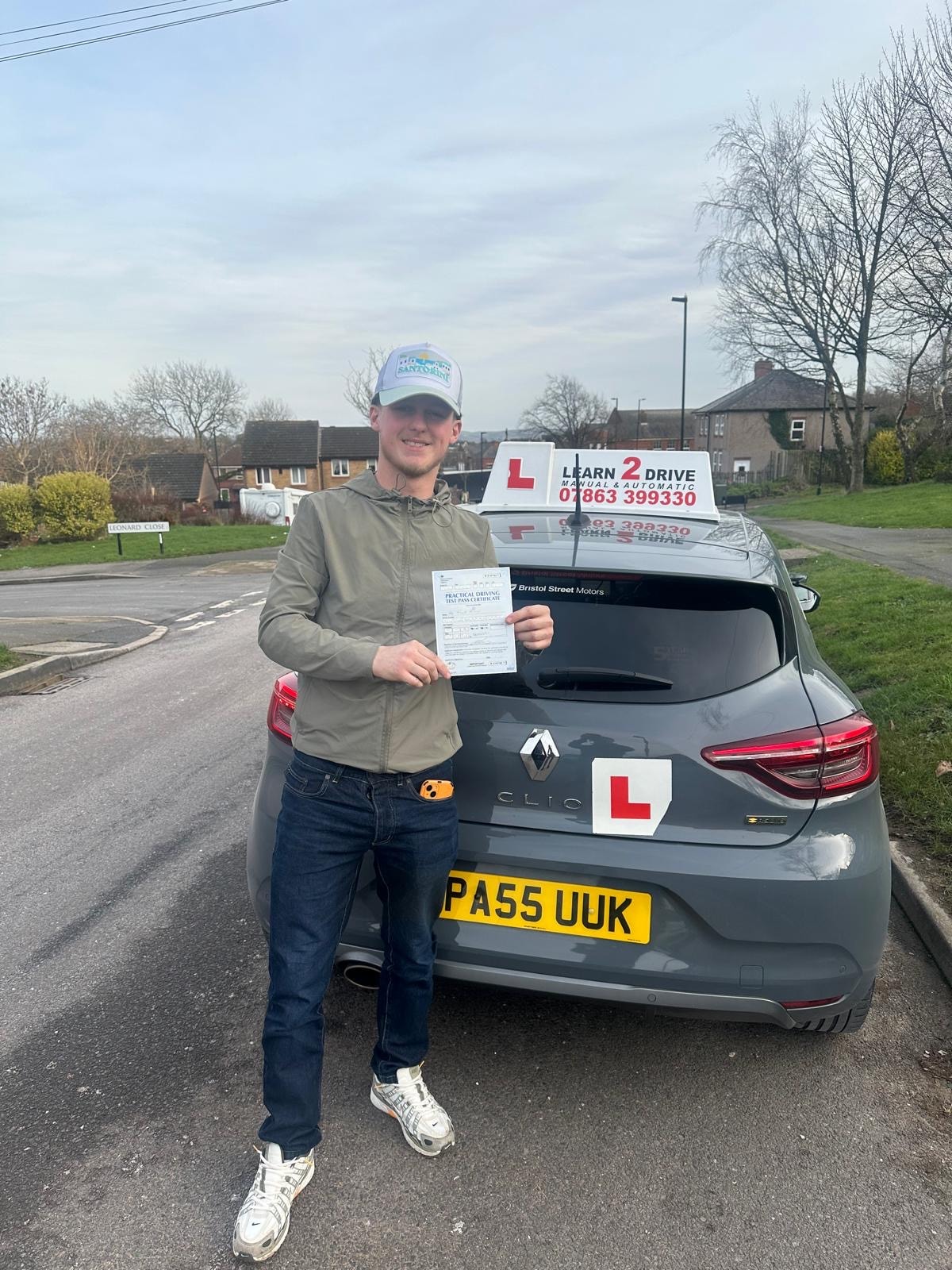 Student holding pass certificate next to a Learn 2 Drive car