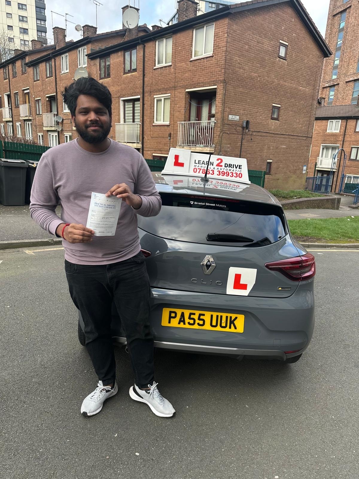 Student holding pass certificate next to a Learn 2 Drive car