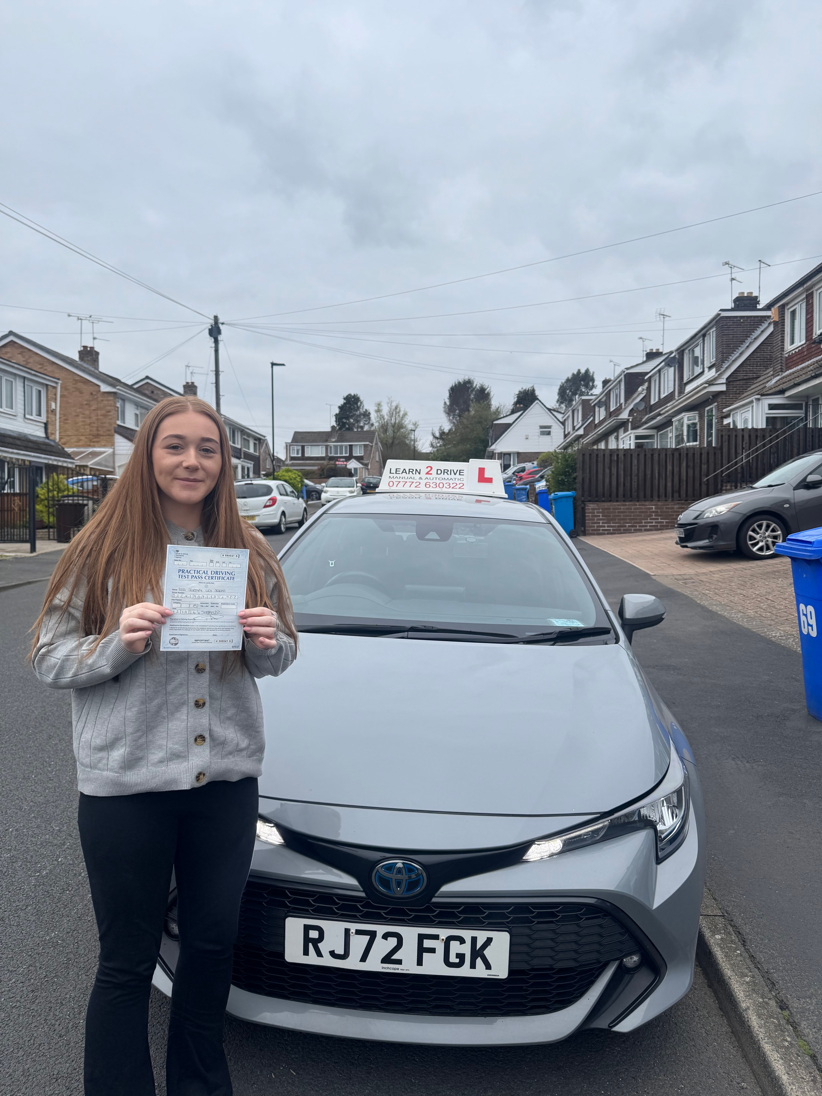 Student holding pass certificate next to Learn 2 Drive car