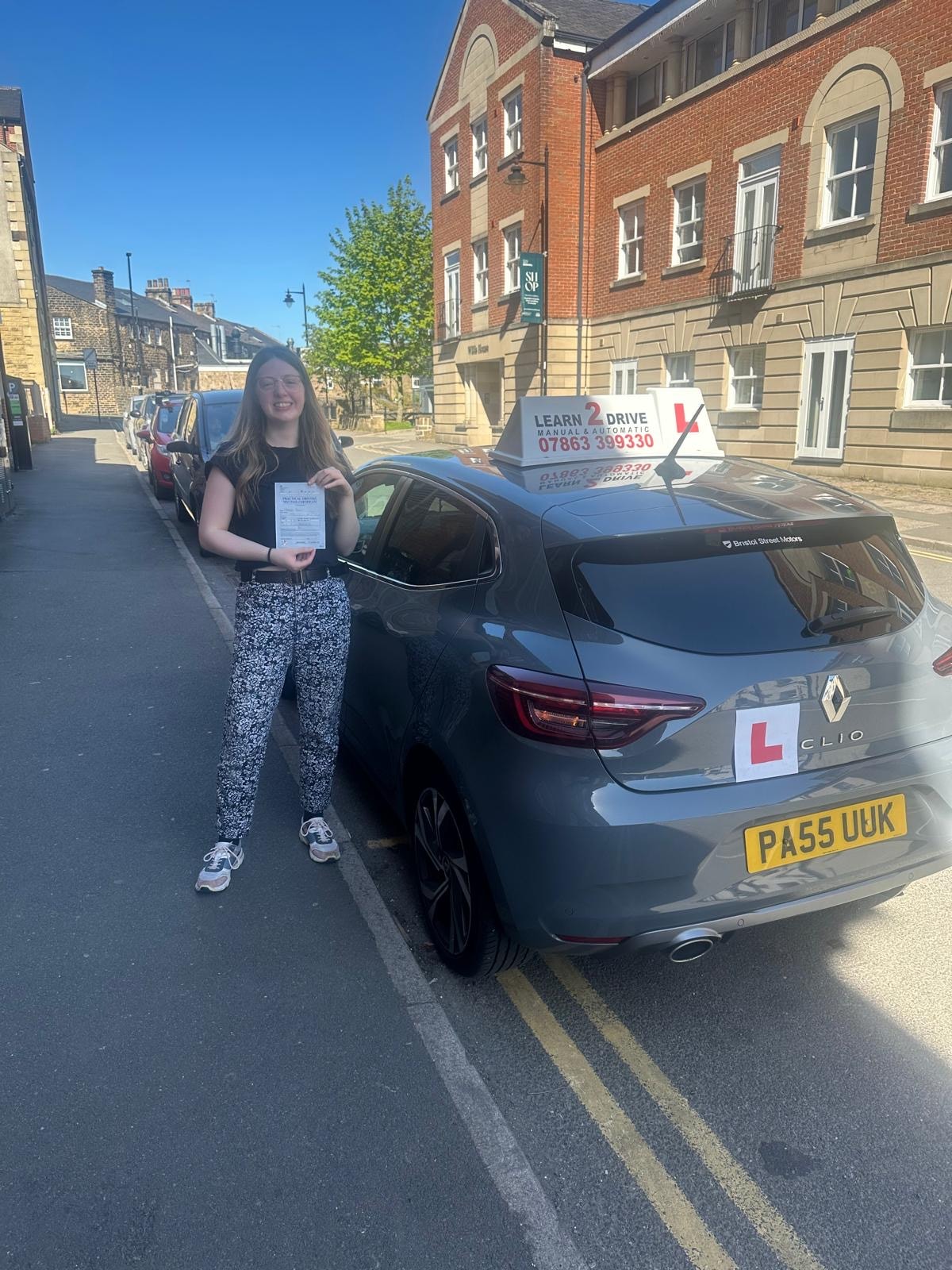Student holding pass certificate next to a Learn 2 Drive car