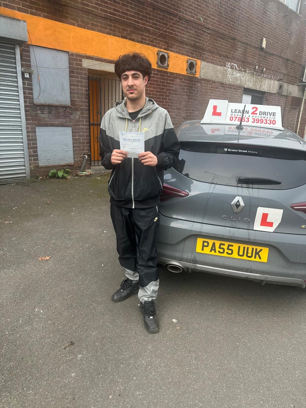 Student holding pass certificate next to a Learn 2 Drive car